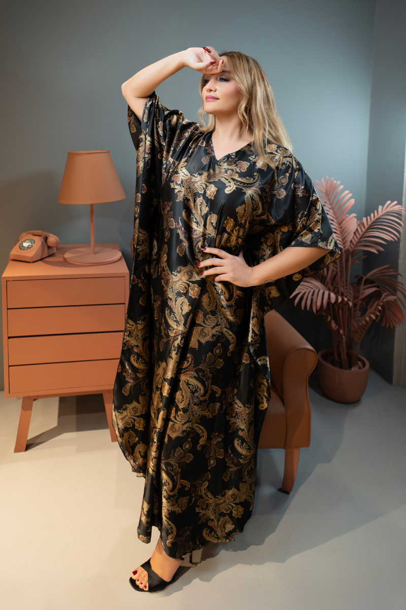 Woman in a long, patterned dress standing in a room with a wooden dresser and plants.