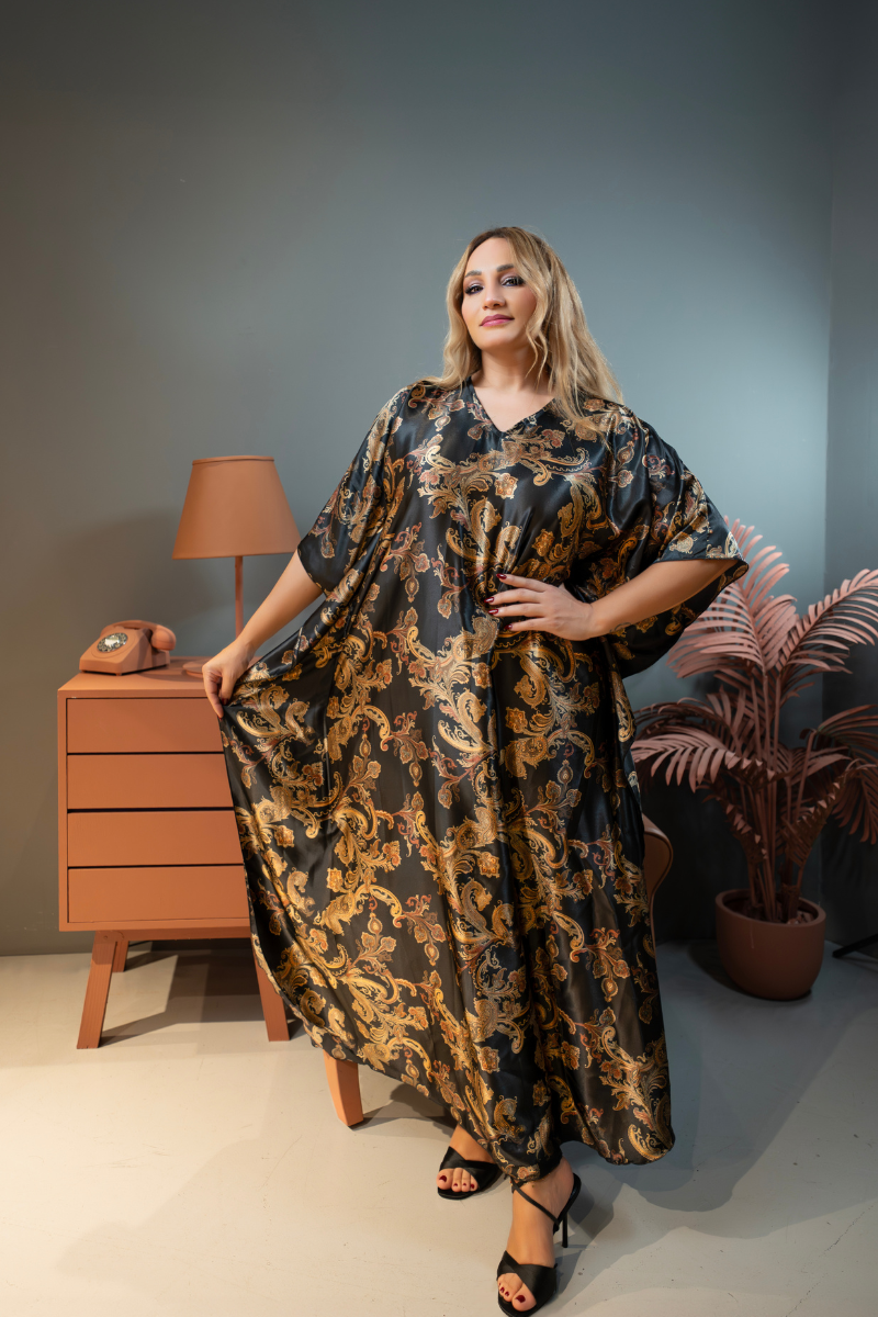 Woman wearing a patterned dress standing in a room with a lamp and plant.