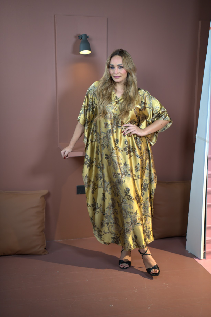 Woman in a yellow floral dress standing against a pink wall.