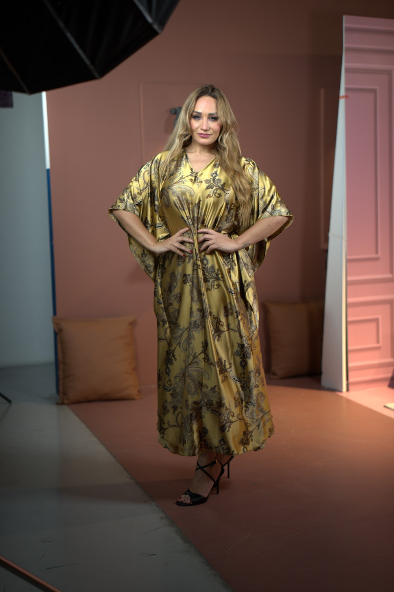 Woman in a yellow patterned dress standing in a studio setting.