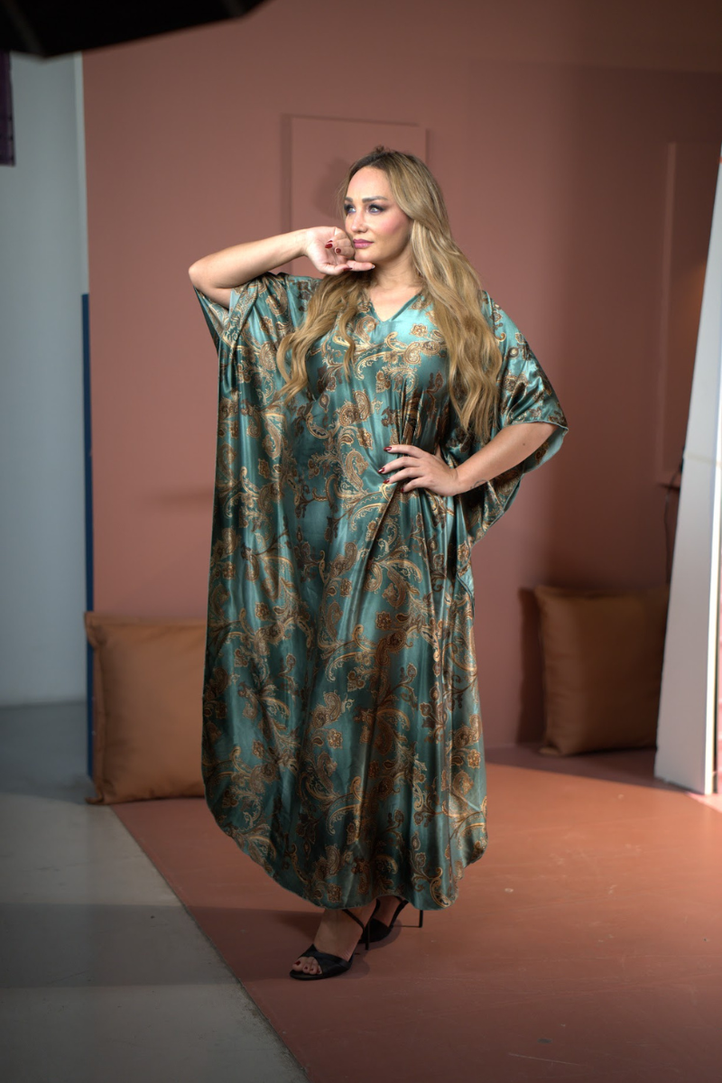 Woman wearing a green patterned dress posing in a room with a pink wall and brown floor.