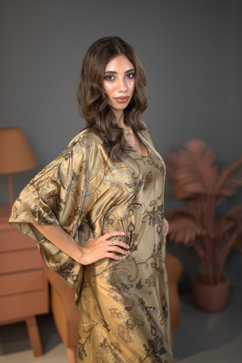 Woman wearing a gold patterned robe in a room with a lamp and plant.