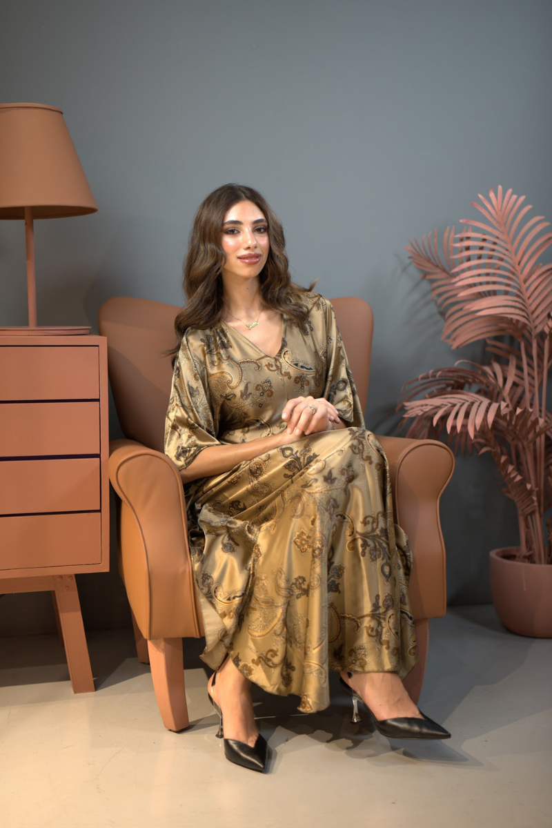 Woman in a patterned dress sitting on a brown armchair with a lamp and plant in the background.