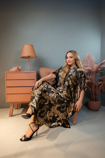 Woman in a floral dress sitting on a chair in a room with a lamp and plant.