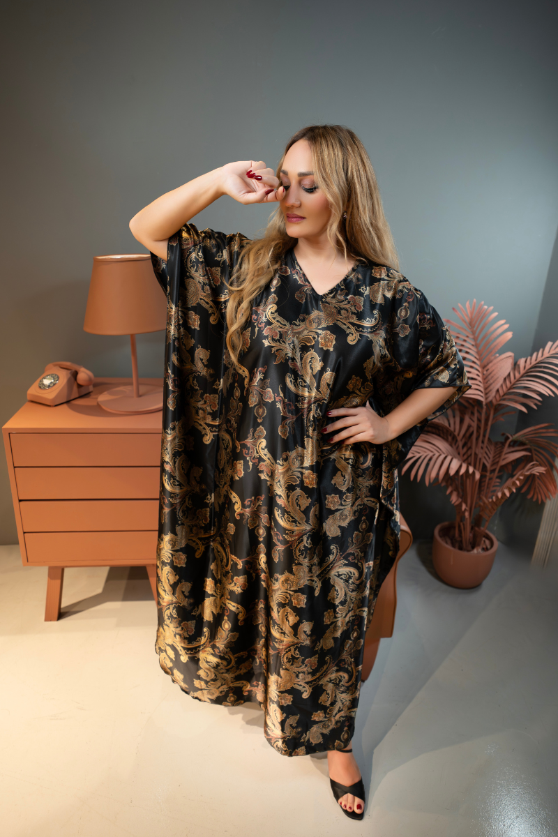 Woman wearing a black floral dress in a room with a lamp and plant.