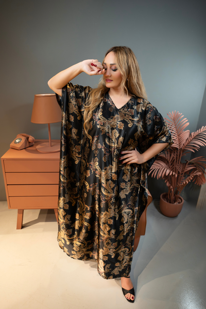 Woman wearing a black floral dress in a room with a lamp and plant.