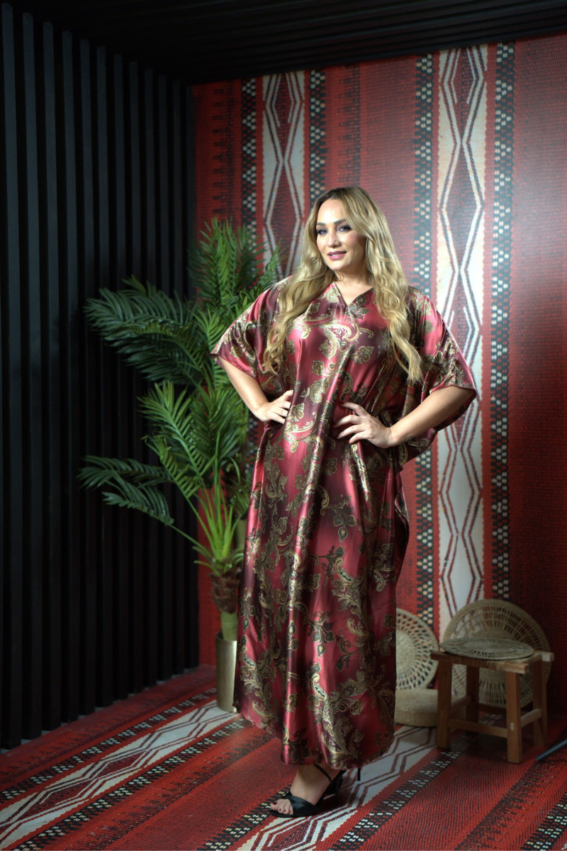 Woman in a patterned dress standing in a room with decorative walls and a plant.