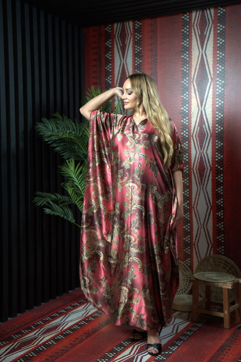 Woman wearing a red patterned dress standing in a room with a decorative wall and rug.