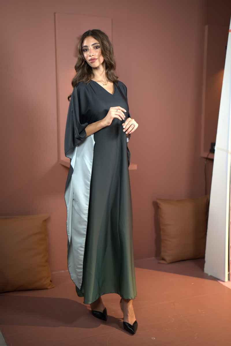 Woman wearing a long, dark green dress with a matching shawl in a room with brown walls and a brown pillow.