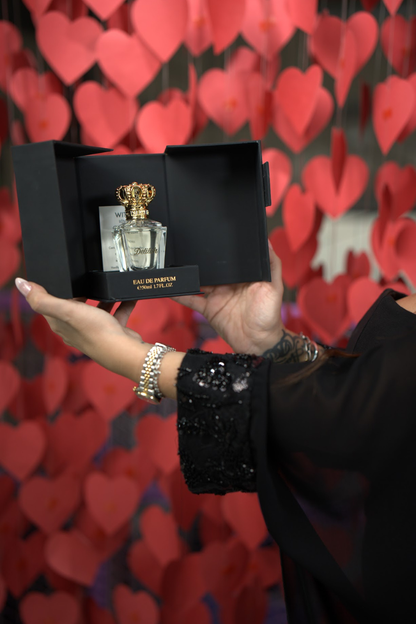 Hand holding a Cartier perfume bottle in front of a heart-patterned background