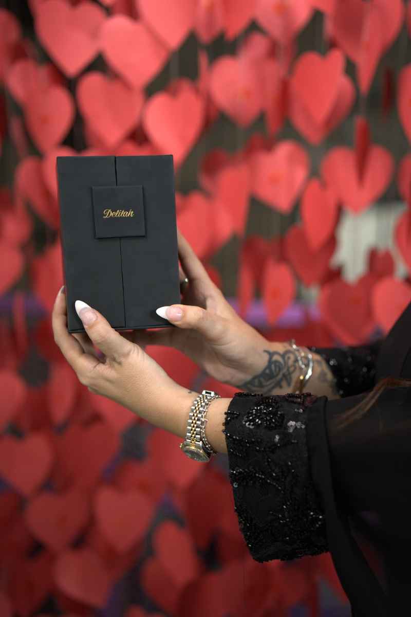 Person holding a black box with gold text against a heart-patterned background
