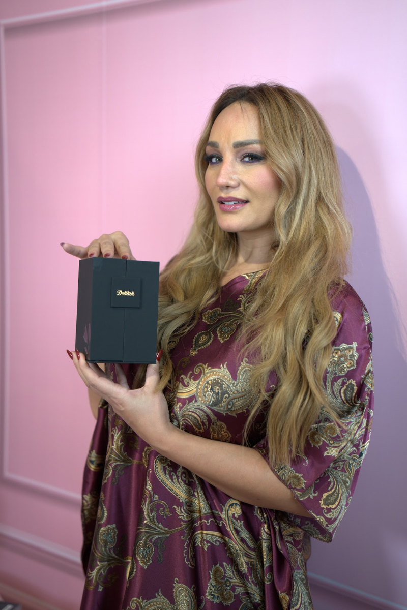 Woman holding a black box with a brand logo against a pink background