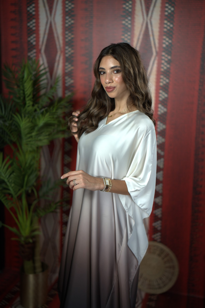Woman in a white dress standing against a patterned red wall.