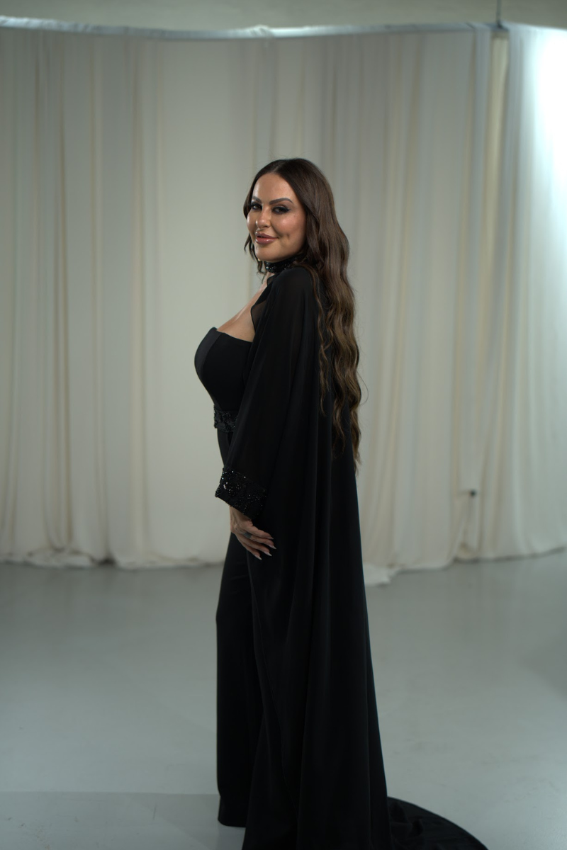 Woman in a black dress standing against a white curtain backdrop