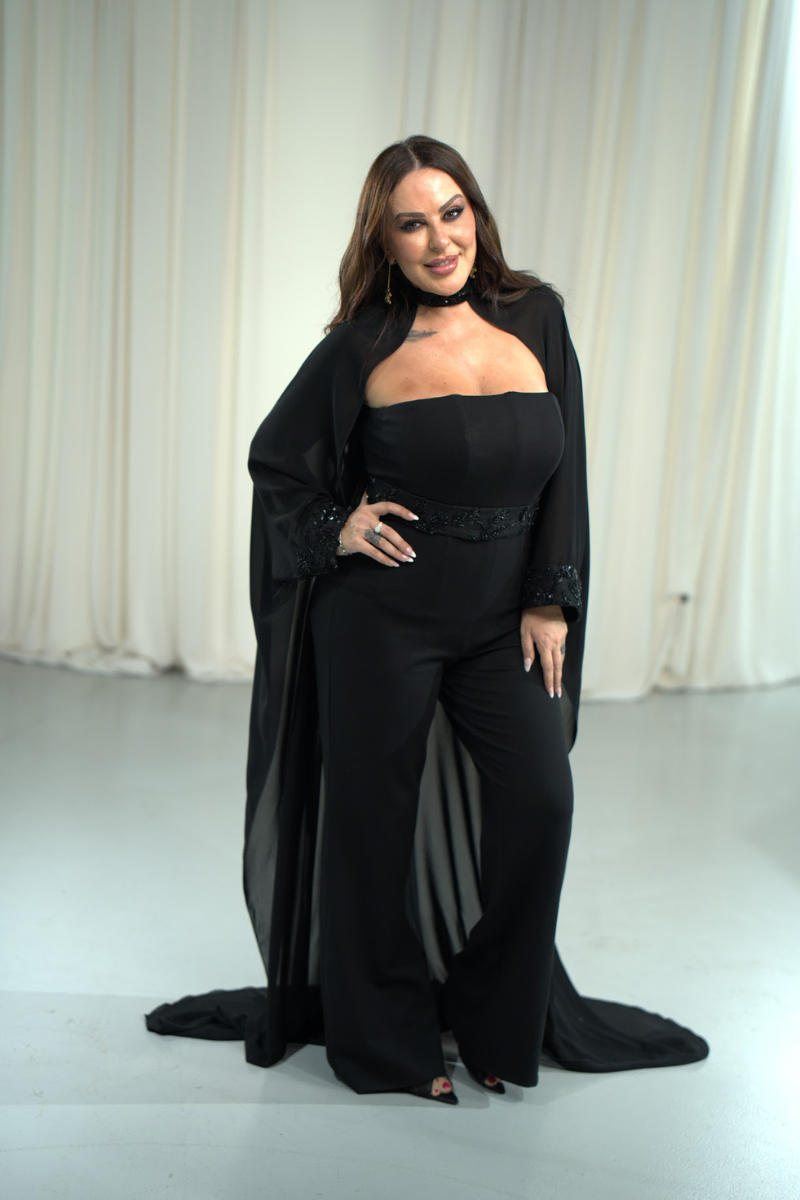 Woman wearing a black outfit with a long jacket against a white curtain background